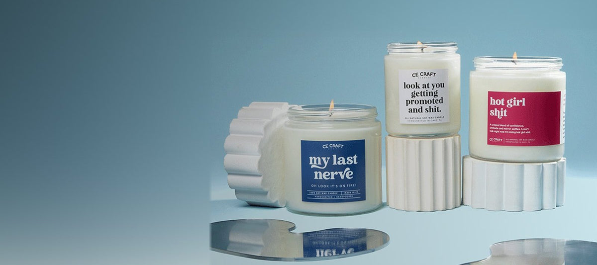 Three C&E candles on white stands against a soft blue backdrop